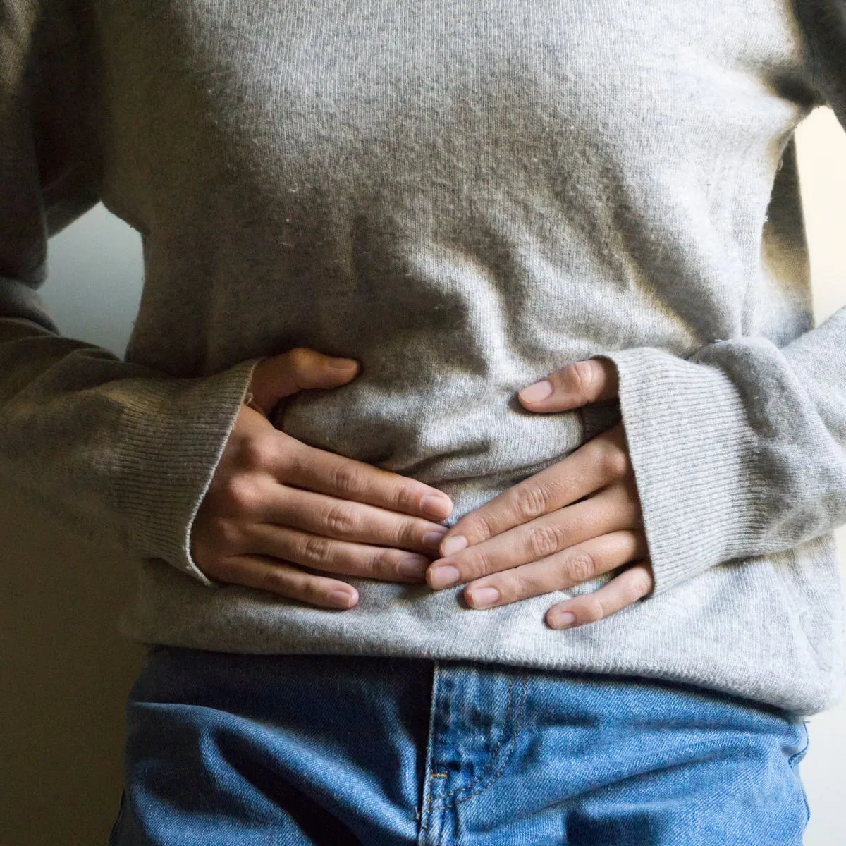 Frau hält sich den Bauch wegen Schmerzen – Sinnbild für chronische Beschwerden (Müdigkeit, Verdauung, Zyklus) - Hausarztpraxis Enge Zürich